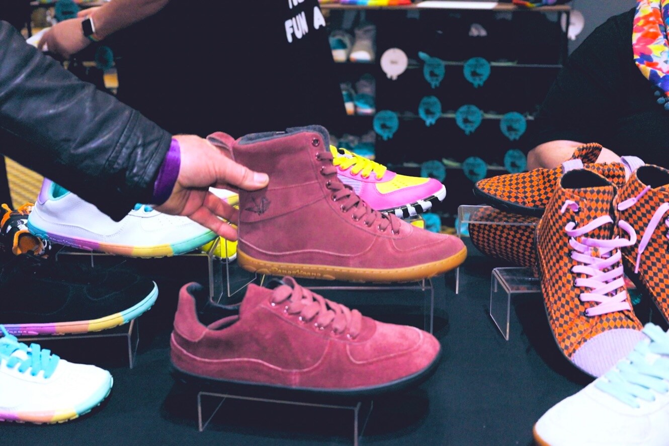 A visitor examining a burgundy boot beside colourful barefoot shoes, photo by The Foot Collective